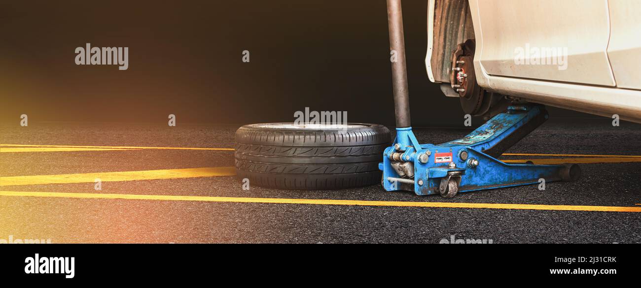 White automobile are lifted by a car jack and a wheel set on an asphalt ...