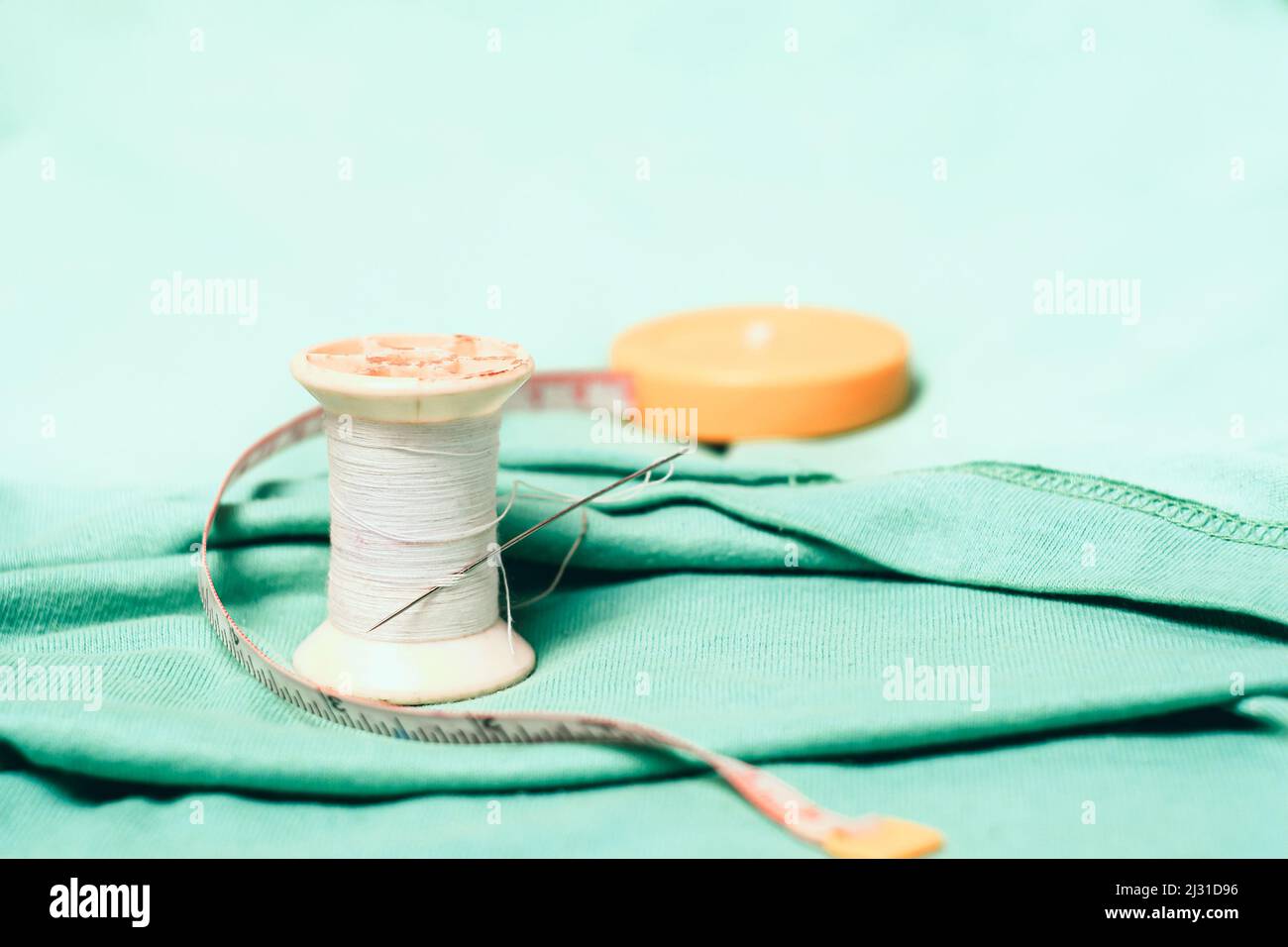 Spool of thread and sewing needle,measuring tape on the cotton cloth ...