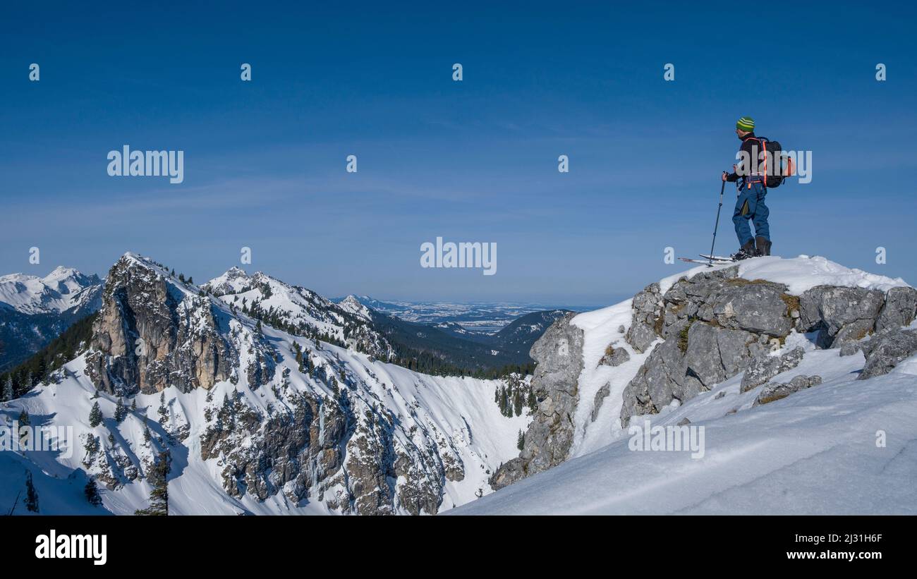 Man rocks at Teufelstaettkopf in winter on ski tour and looks over the snowy mountains of the Ammergau Alps in Bavaria in winter Stock Photo