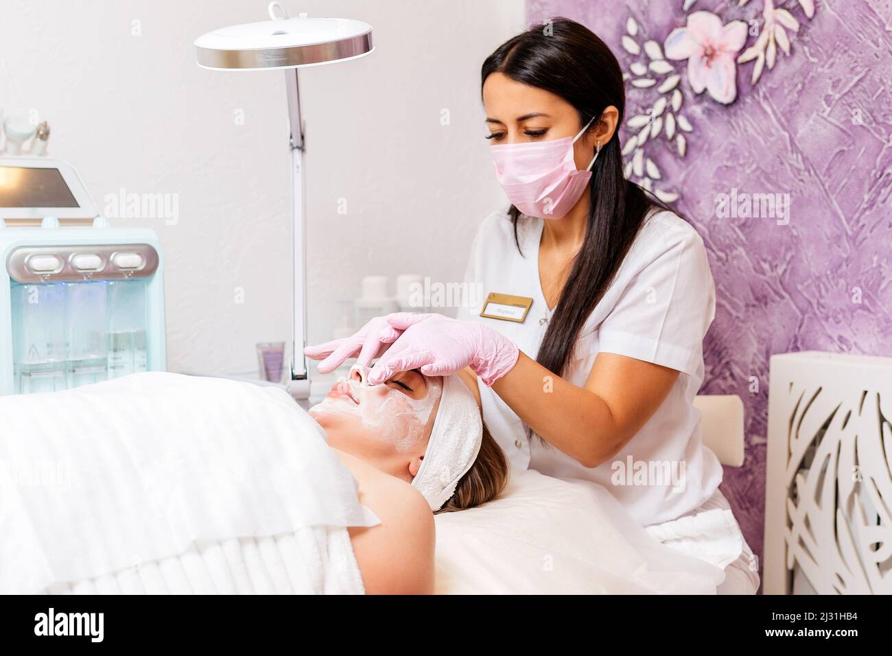 Female cosmetologist at protective mask and medical gloves massages