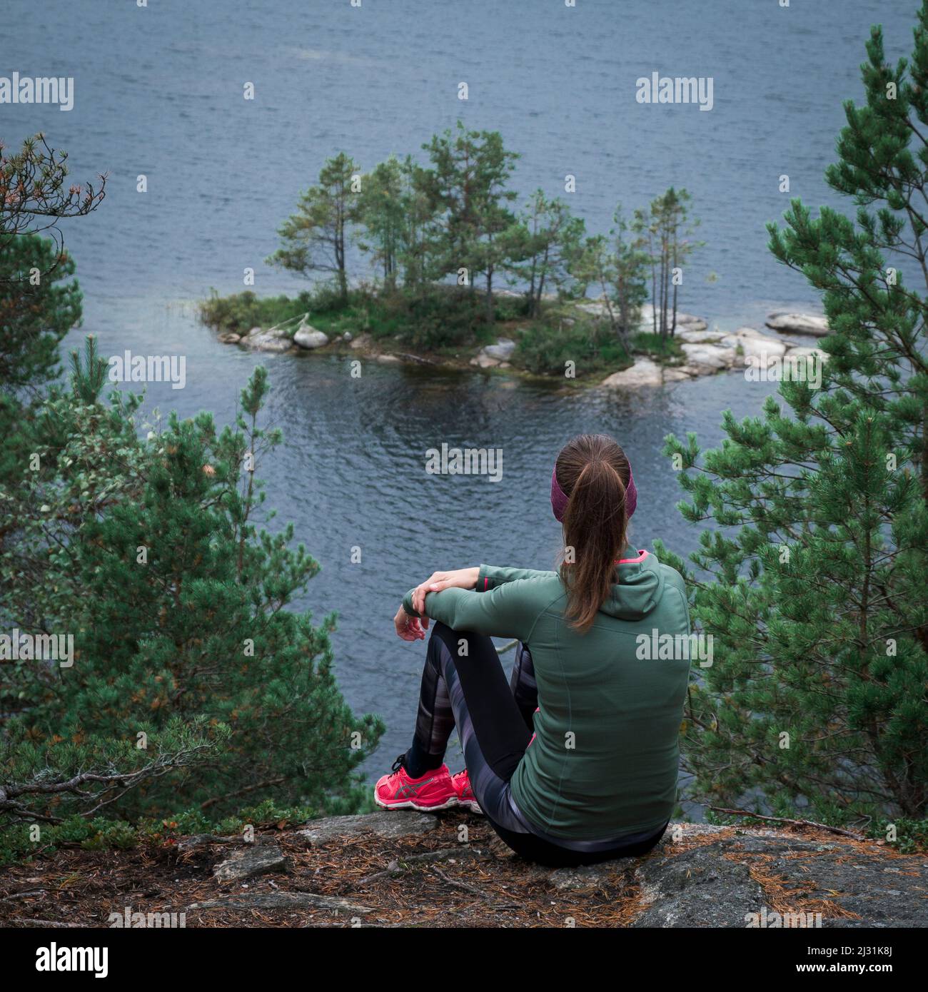 Woman while hiking looks out over small island in lake Stensjön in Tyresta National Park in Sweden Stock Photo