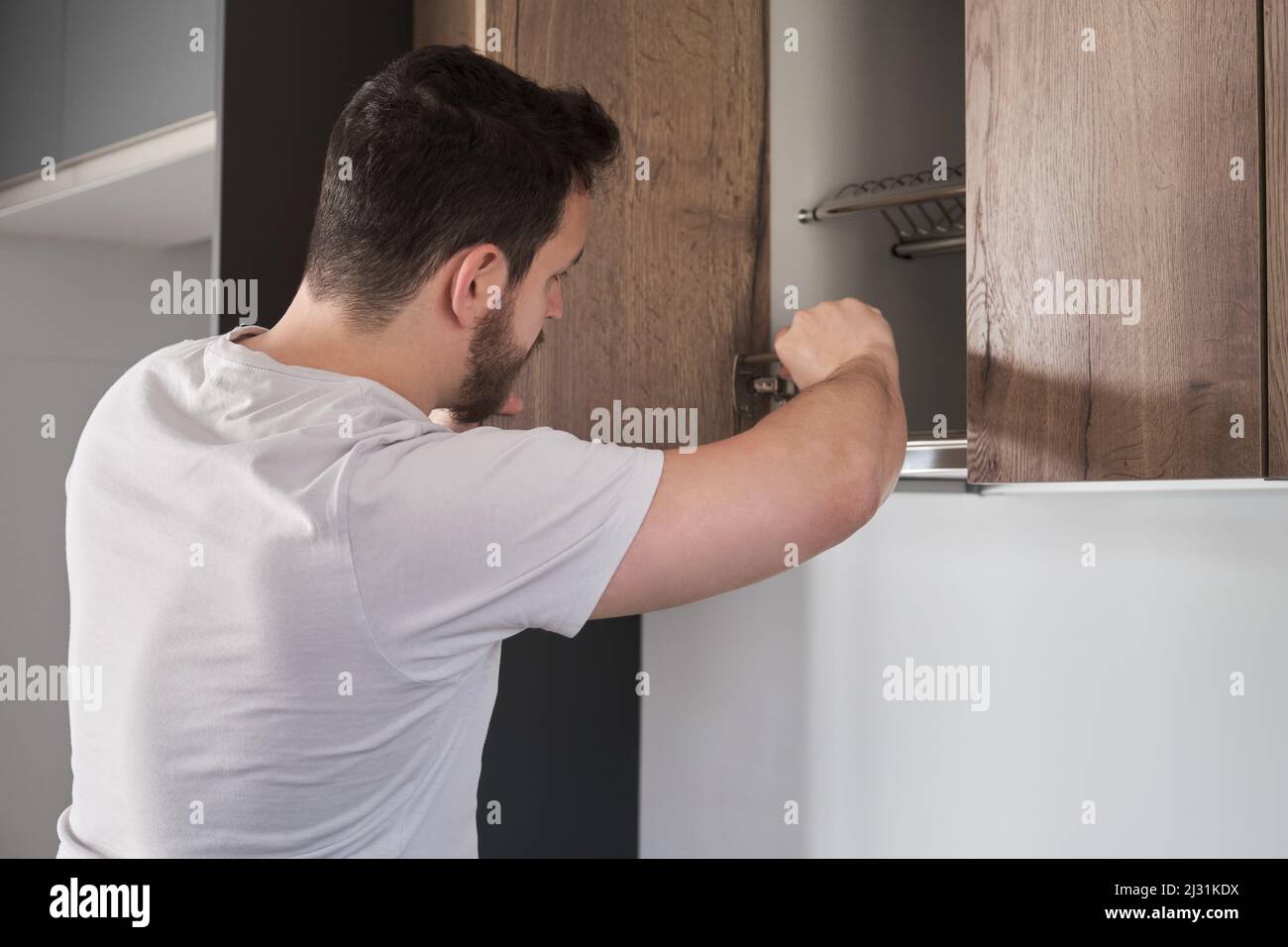 Young latin man installing cupboard in the kitchen using a screwdriver. Stock Photo