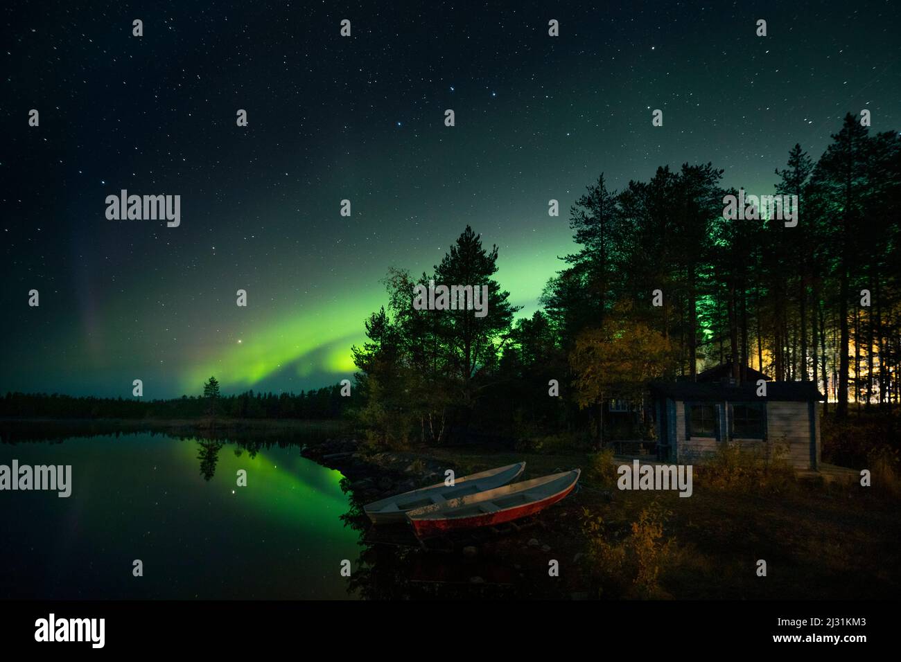 Northern lights in the night sky on the lakeshore with hut and boats in Lapland, Sweden Stock Photo