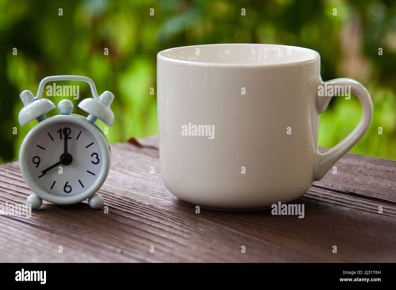 Alarm clock pointing at 8 o'clock with coffee cup on a bench. Copy
