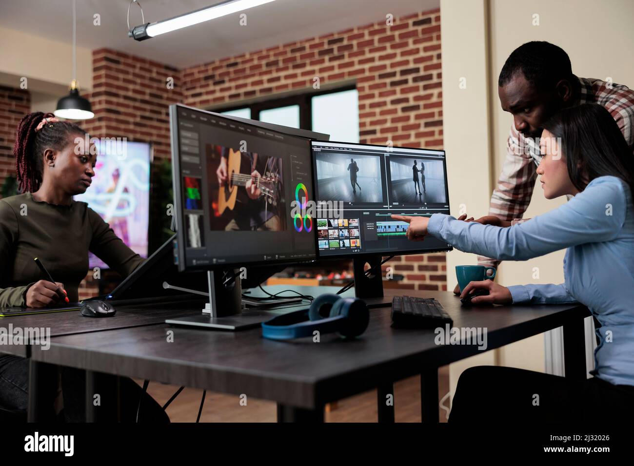 Professional videographer sitting at desk while coworker helping her