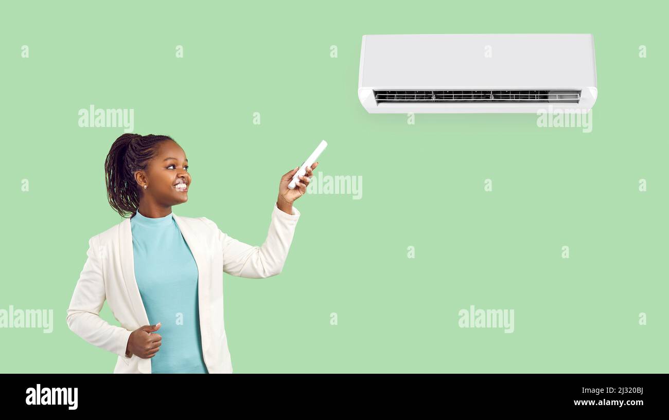 Woman with remote control standing near air conditioner isolated on light green background. Stock Photo