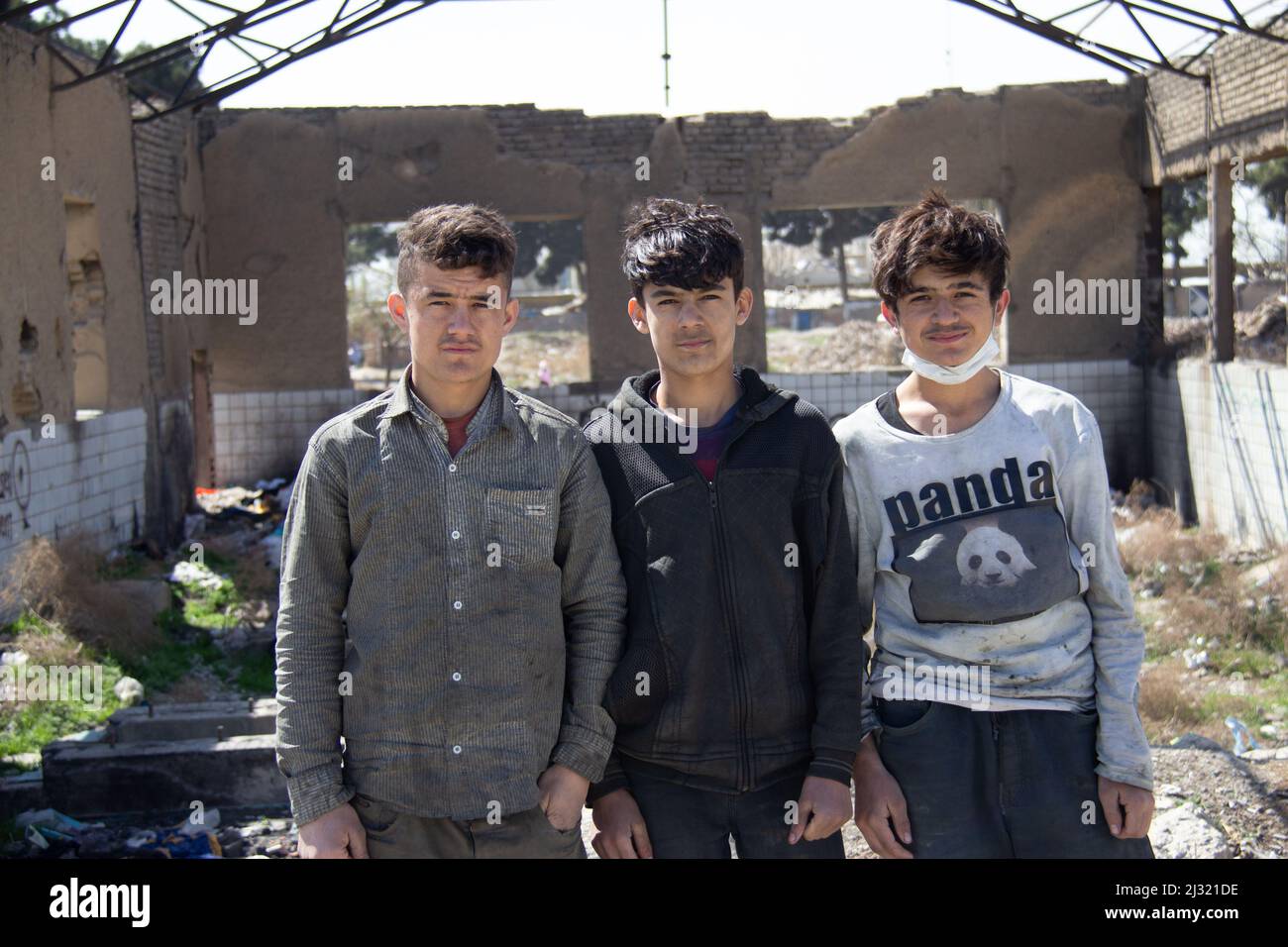 Three Afghan refugees are standing in a ruin in Tehran for a photographer to photograph Stock Photo