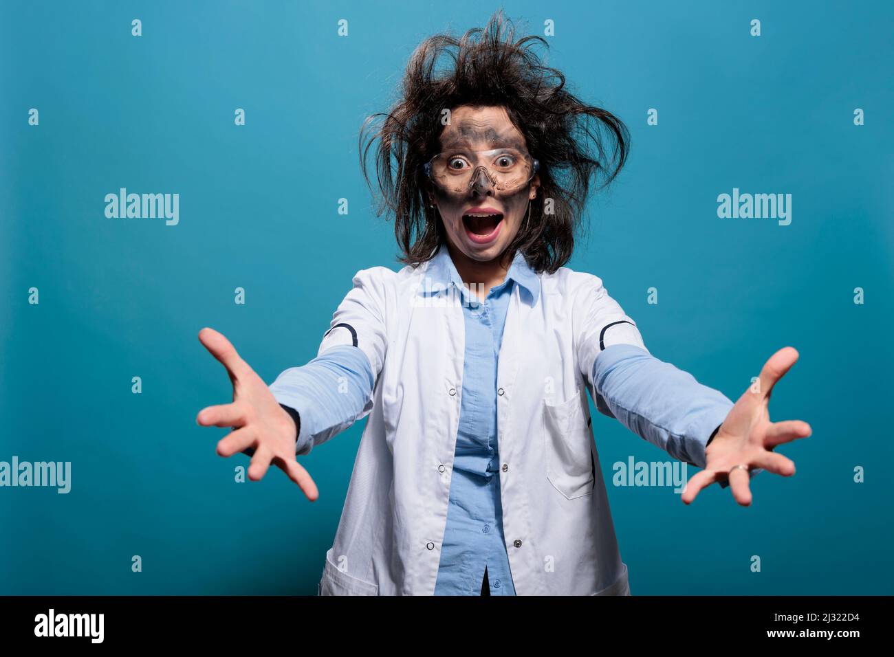Wacky looking insane chemistry scientist yelling in panic with messy hairstyle and dirty face amazed by failed experiment explosion. Teriffied strange looking weirdo chemist on blue background. Stock Photo
