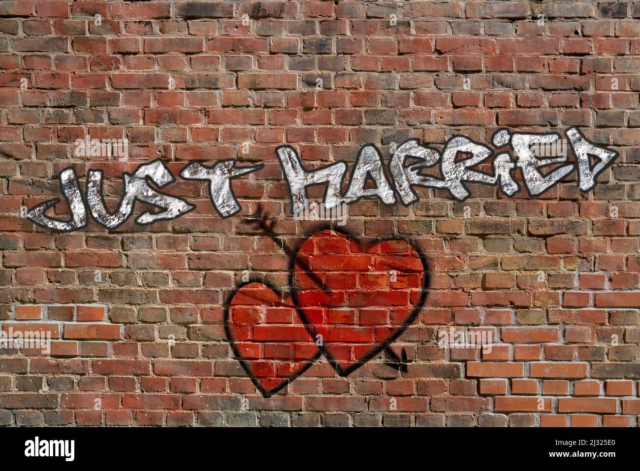 Silver Just Married graffiti with to sprayed red hearts on red brick wall Stock Photo