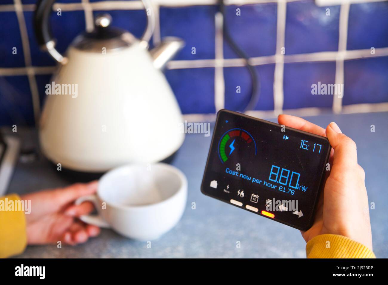Person viewing a smart meter and making a hot drink, with a white kettle Stock Photo