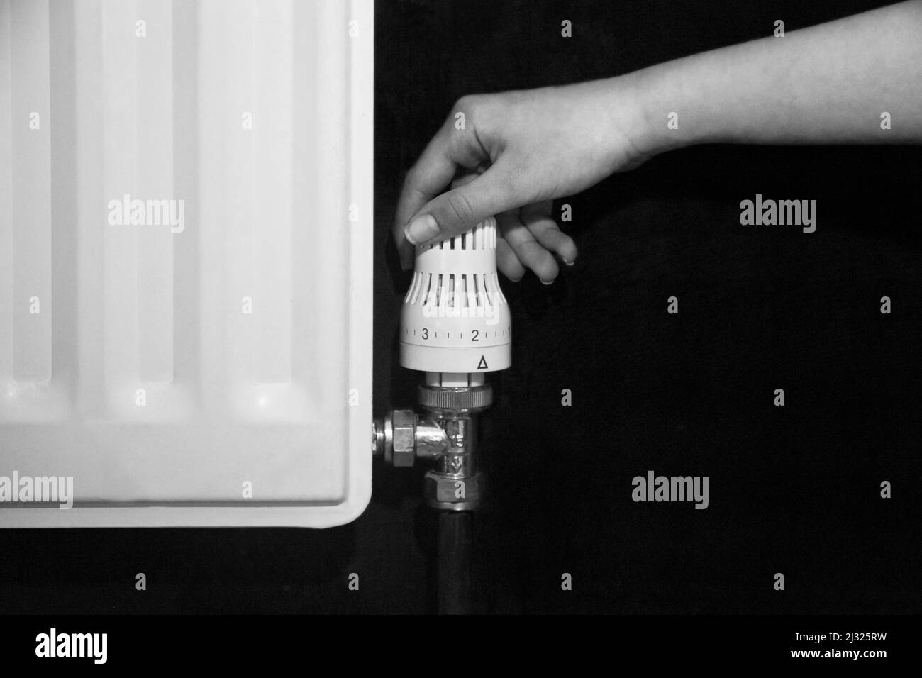 Hand turning down the control valve of a radiator, in black and white Stock Photo
