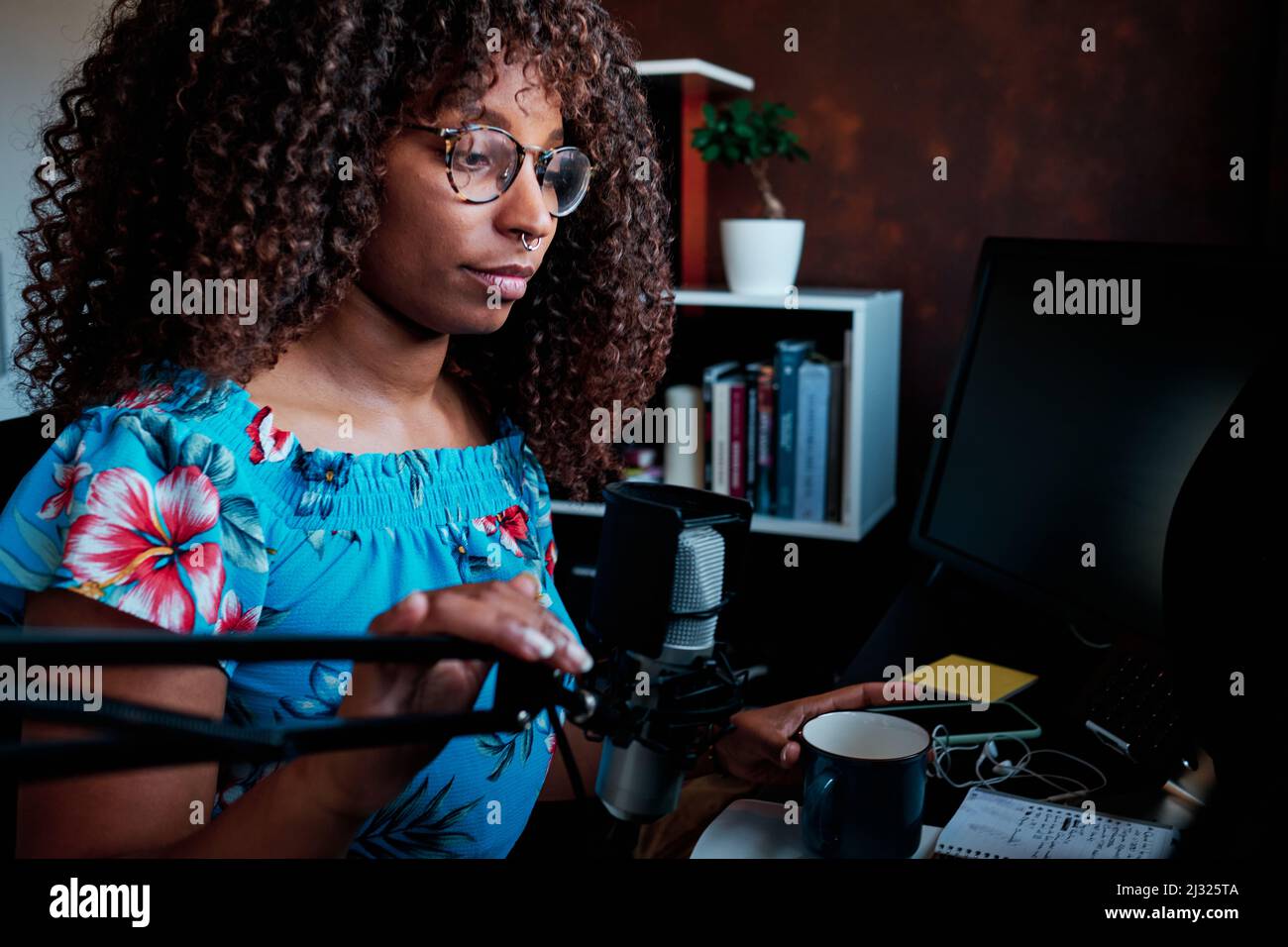 Young curly hair black woman podcasting with microphone at the computer Stock Photo