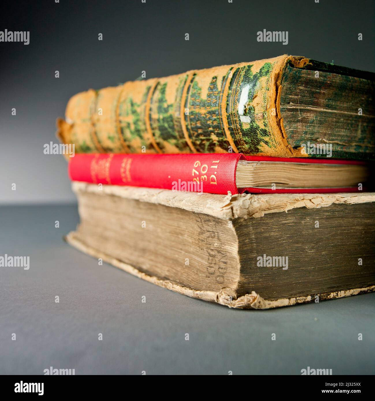 Three old books, stacked on top of each other, on a grey background Stock Photo