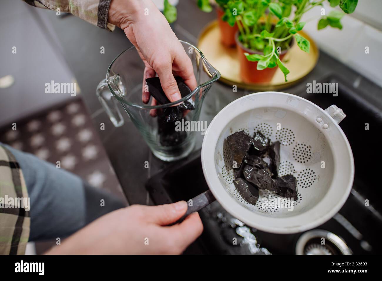 Woman cleaning shungite stones in sieve with pouring water in sink
