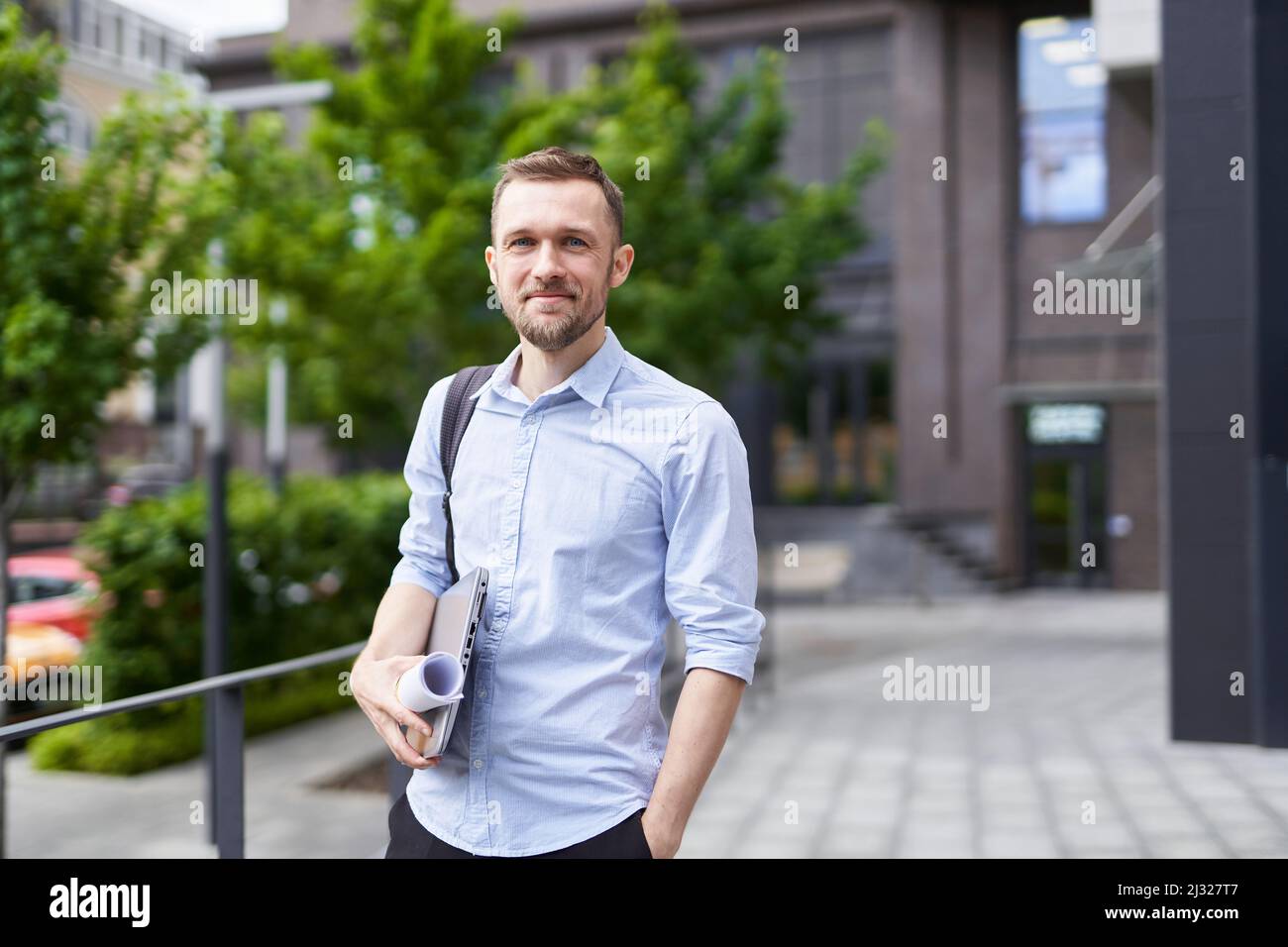 Portrait of successful and confident real estate agent, businessman or financial manager. Smiling successful stylish bearded business man standing on a street with urban background. High quality image Stock Photo