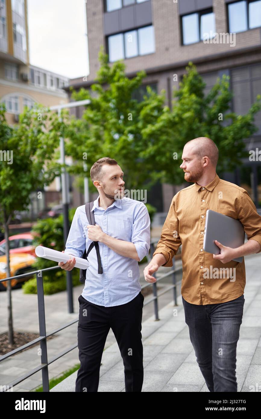 Business people or real estate agents talking outdoor modern building background. Construction, architecture or design managers concept. On the go meeting in downtown near office. High quality image Stock Photo