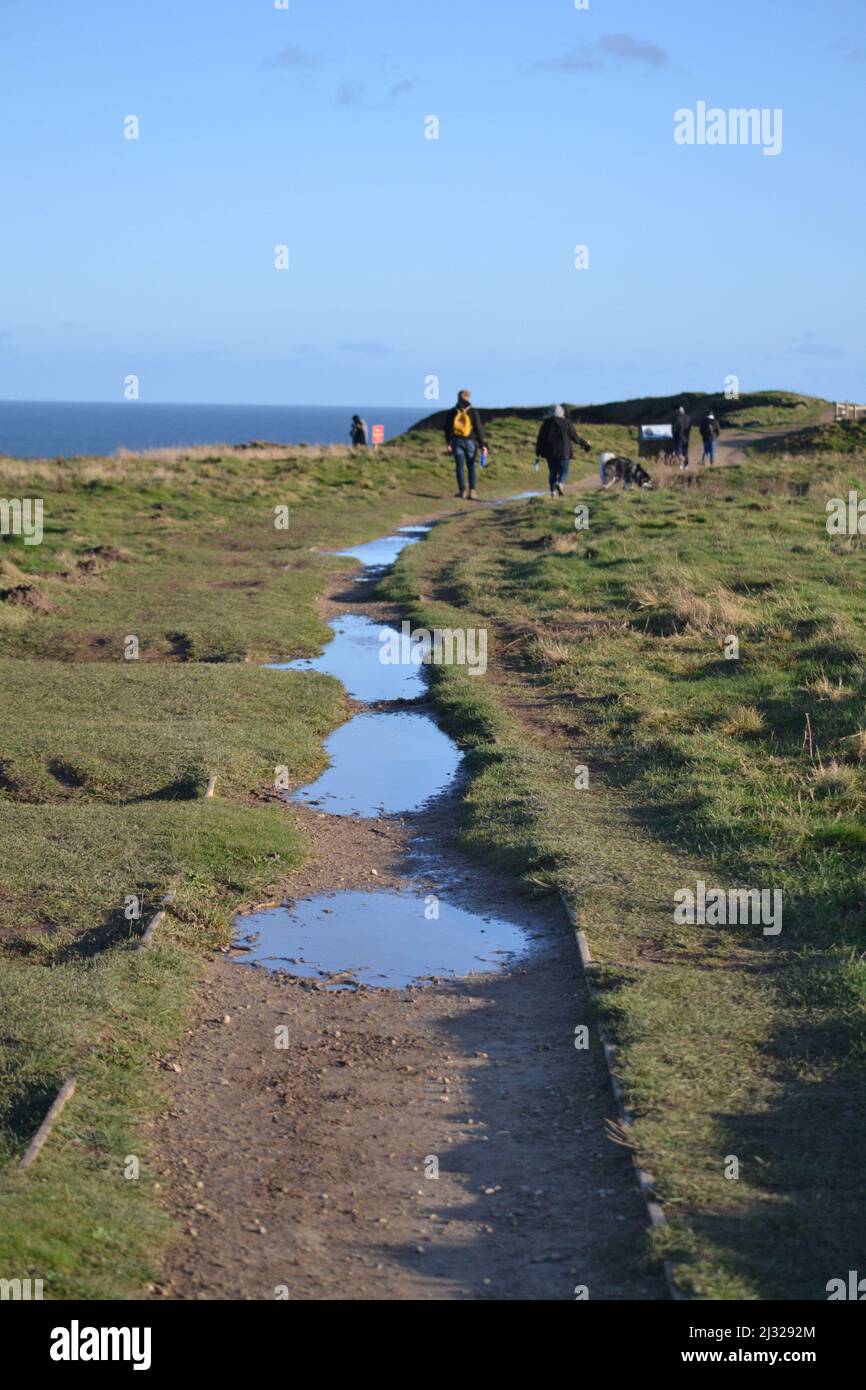 Puddles On Footpath Along Filey Brigg - Bright Sunny Winters Day - Blue Sky Reflecting In Puddles - North Yorkshire - UK Stock Photo
