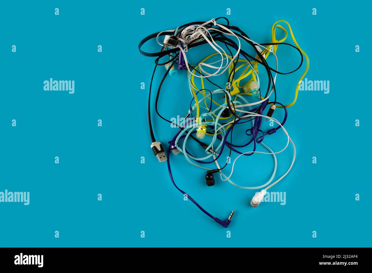 A lot of tangled headphones for smartphone on a blue background. Stock Photo