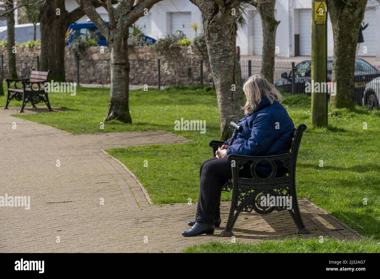 A mature woman sitting alone on a park bench in Trenance Gardens in Newquay in Cornwall in the UK. Stock Photo