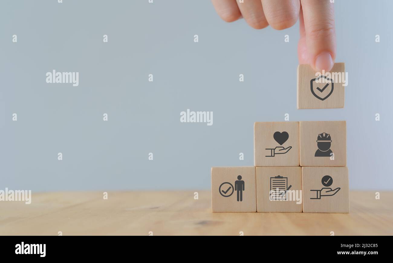 Safety at work concept. Hand holds wooden cube with safety icons; safety first, protections, health, regulations and insurance.  Used for banner, beau Stock Photo