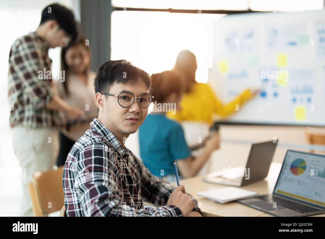 Portrait of young businessman smart casual wear looking at camera and smiling, arms crossed in modern office workplace. Young Asia guy standing in Stock Photo