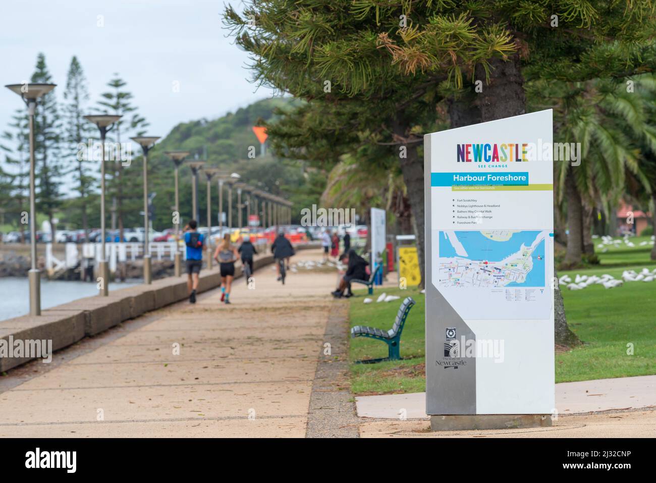 People exercising, walking and riding bicycles along the foreshore footpath near Queens Wharf, Newcastle Harbour towards Nobbys Head in Australia Stock Photo