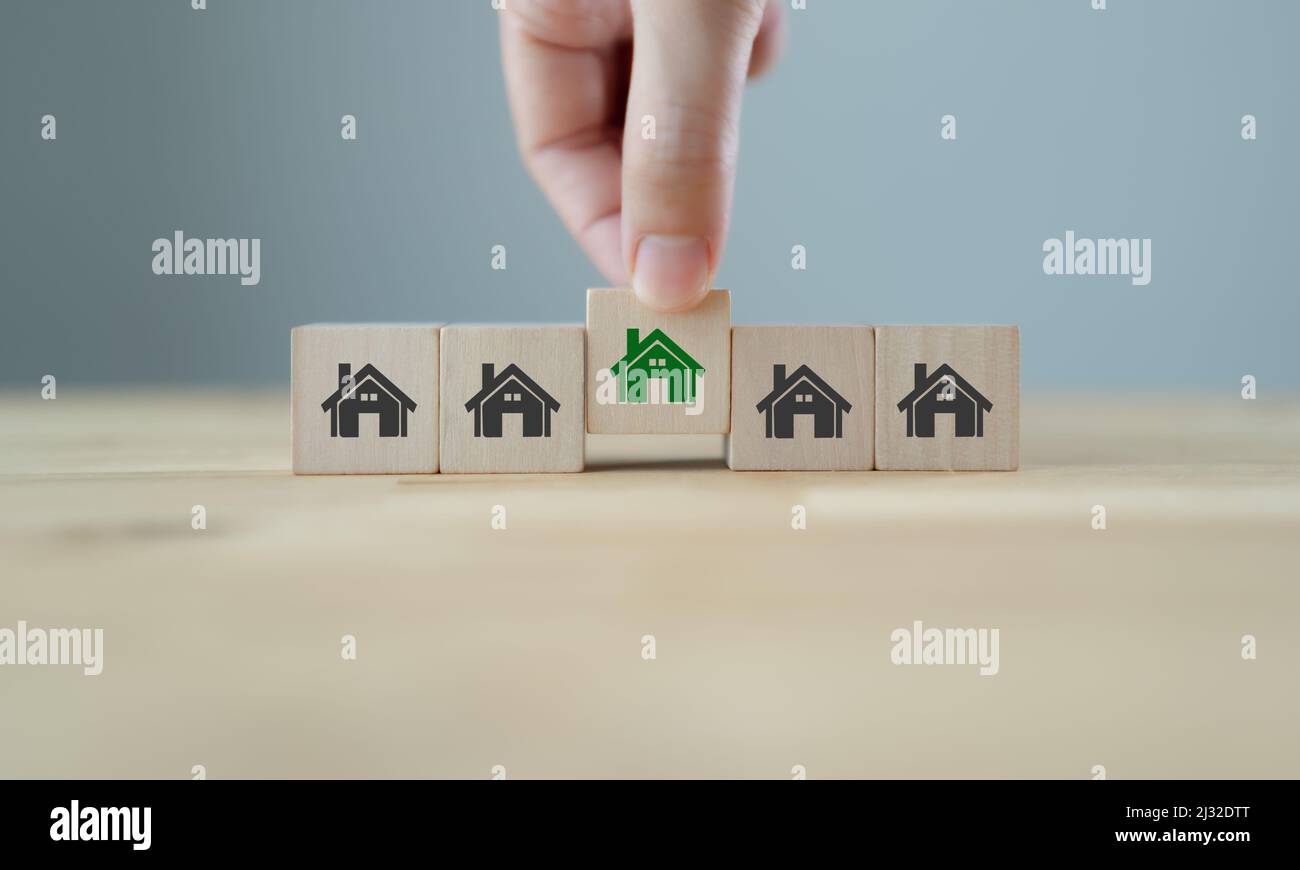 ECO house concept. Smart and sustainable design. Environmentally friendly house. Hand holds wooden cubes with green house symbols on grey background a Stock Photo