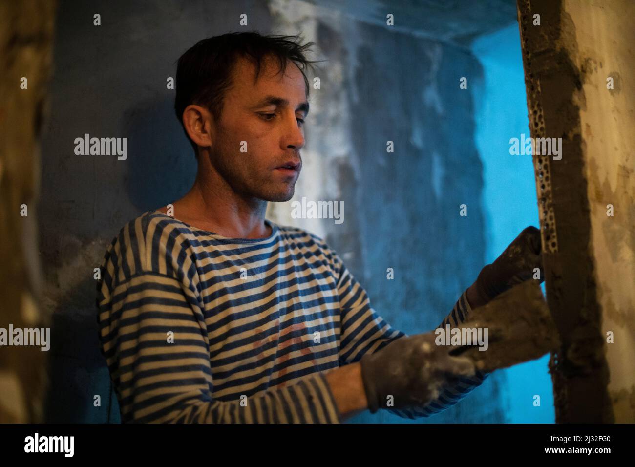 Guy is doing wall repairs. Man makes flat wall. Cement application