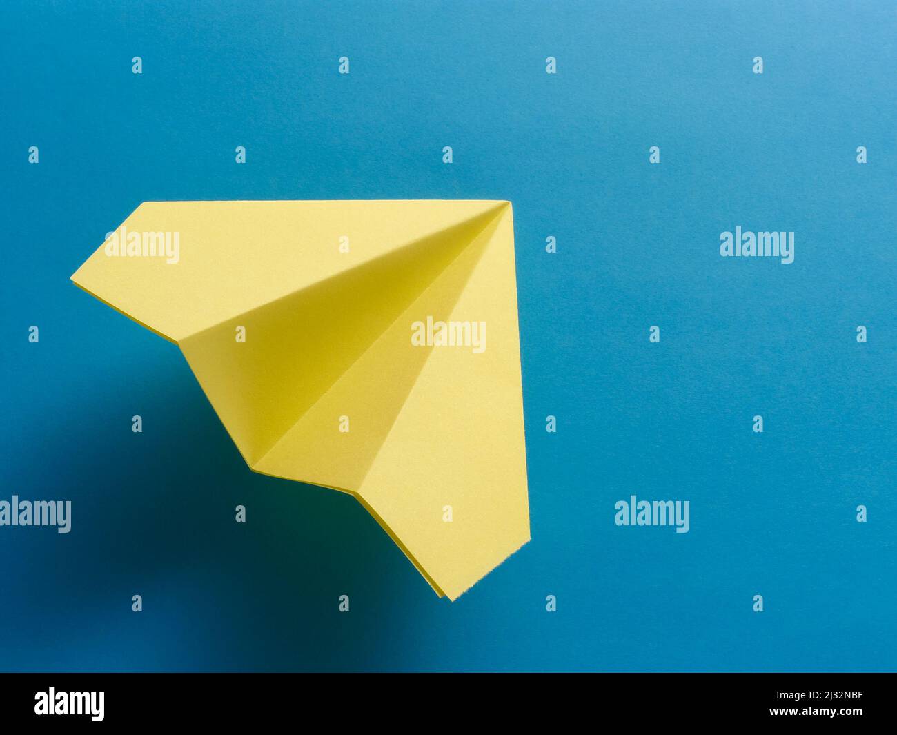 Yellow origami fighter jet on blue background. Stock Photo