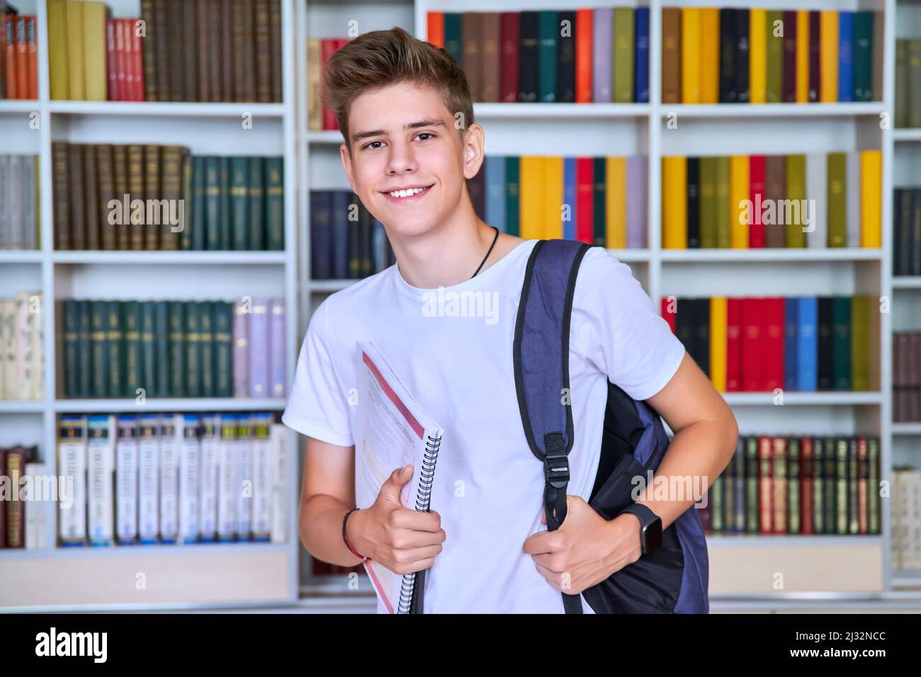 Portrait of male teenage student looking into the camera in library ...