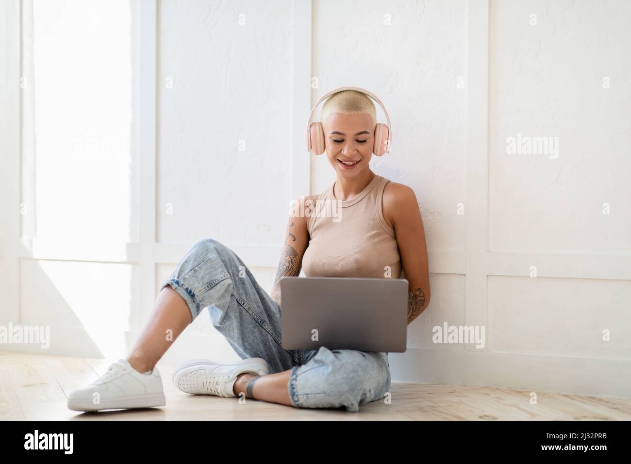 Positive lady in wireless headphones working on laptop, sitting on