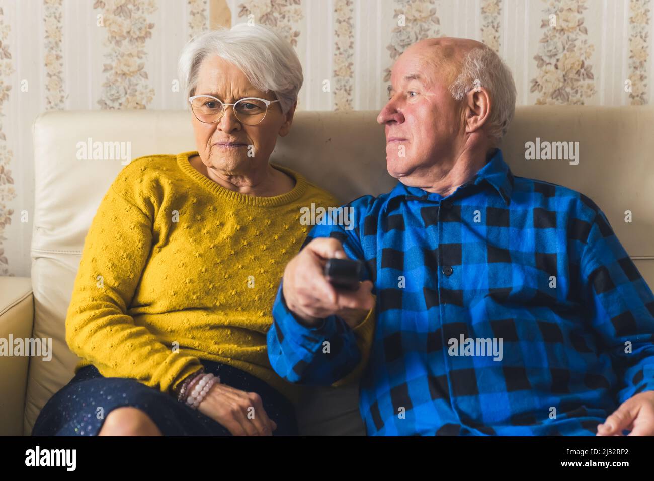 Portrait of an elderly couple watching television while sitting on the sofa - man is holding the remote control. High quality photo Stock Photo