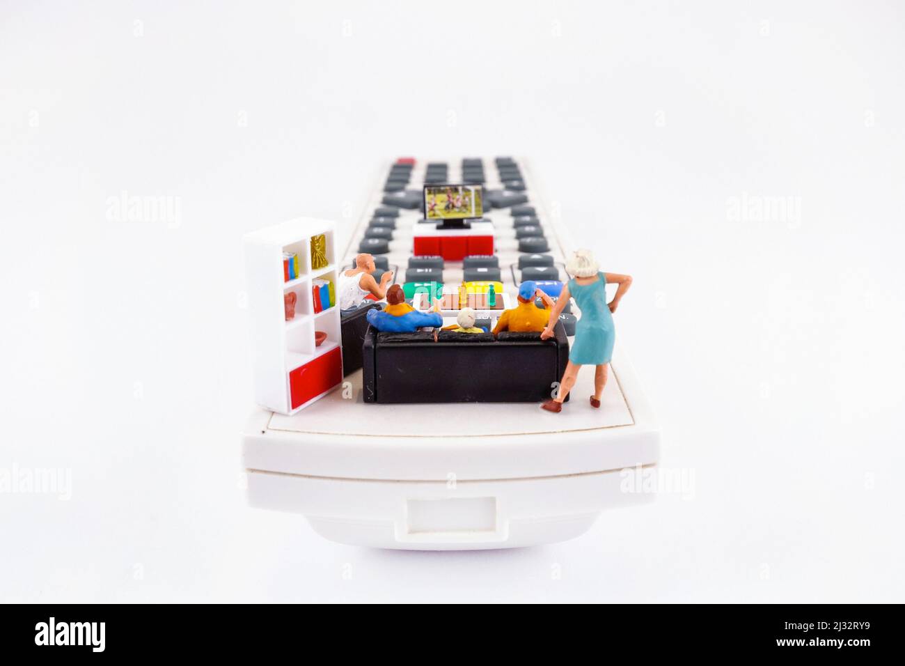 Family spending time together channel surfing and watching a television, conceptual photography. Miniature figurines on the TV remote, watching game Stock Photo