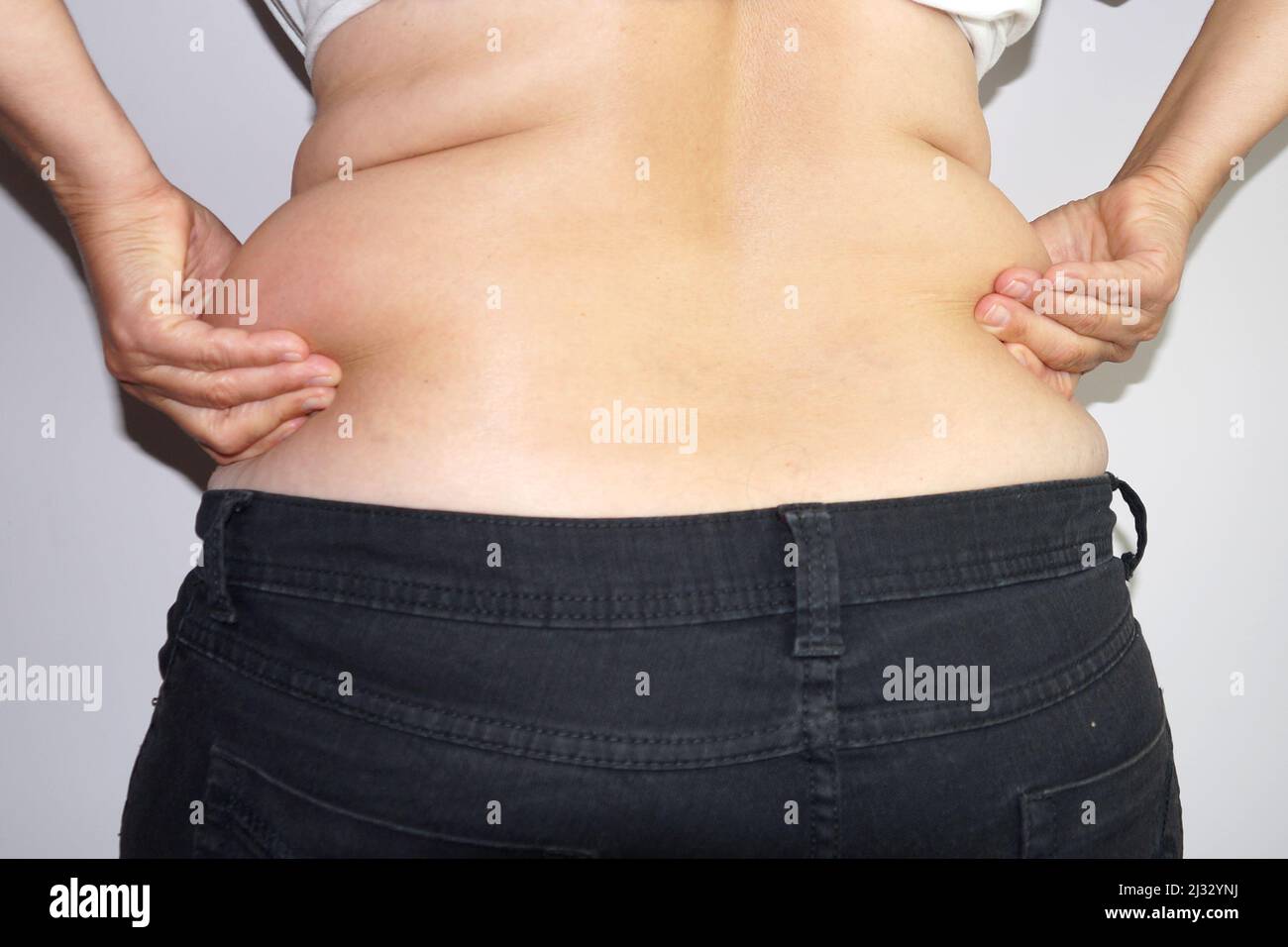 woman in jeans holds fat folds at her waist with her hands, rear view. Stock Photo