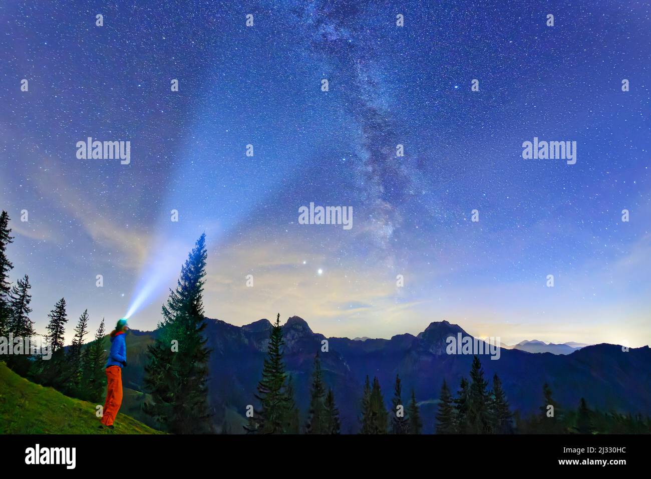 Woman stands at Farrenpoint and shines with lamp on starry sky with Milky Way, Farrenpoint, Mangfall Mountains, Bavarian Alps, Upper Bavaria, Bavaria, Germany Stock Photo