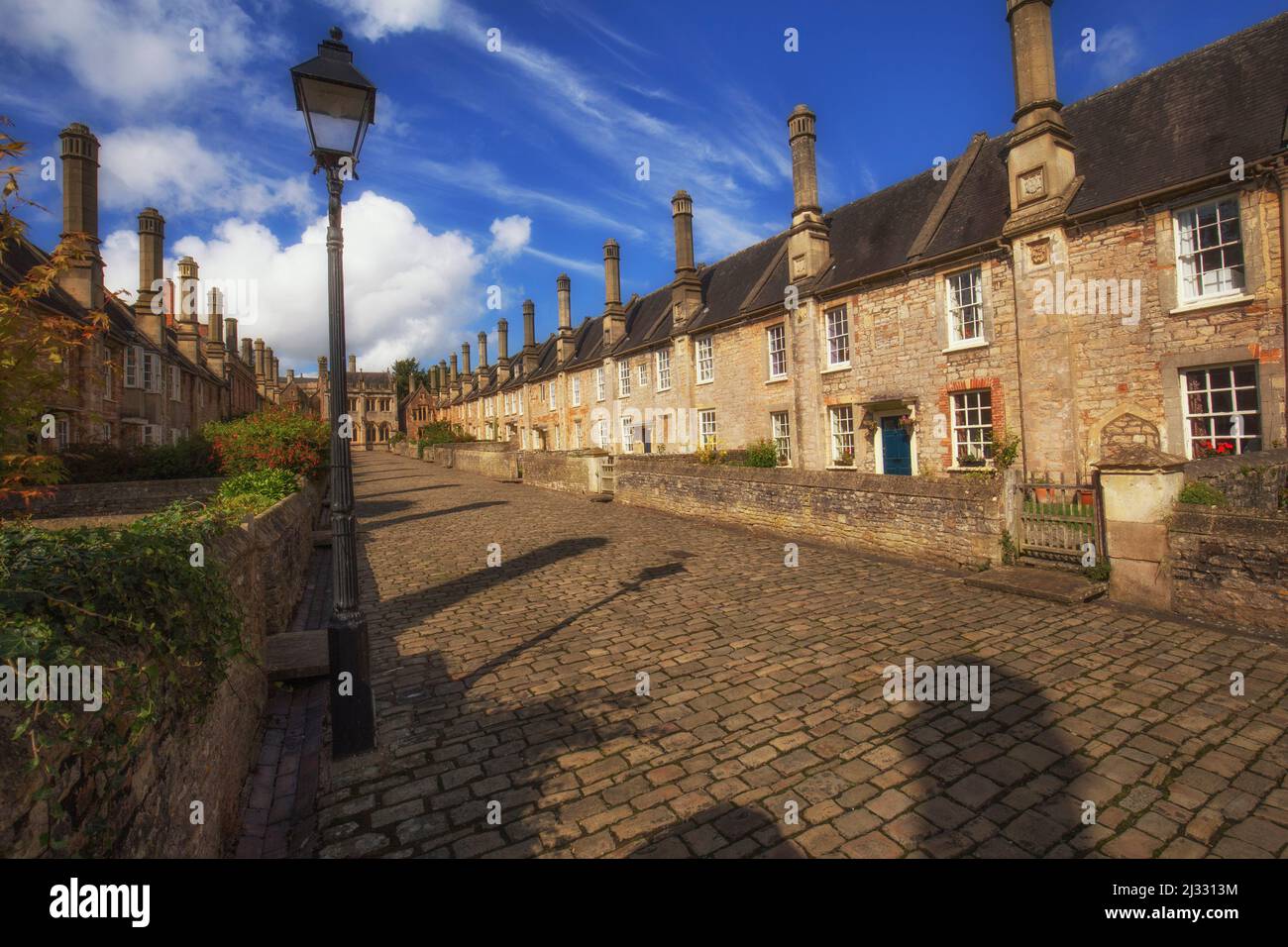 View down the ancient Vicar&#39;s close lane in Wells, Somerset, England in sunshine and puffy clouds. Stock Photo