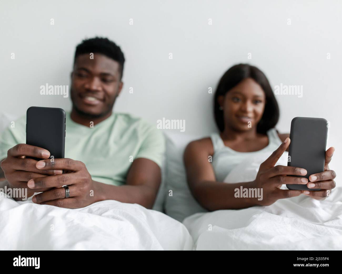 Smiling young african american husband and wife typing on smartphones ...