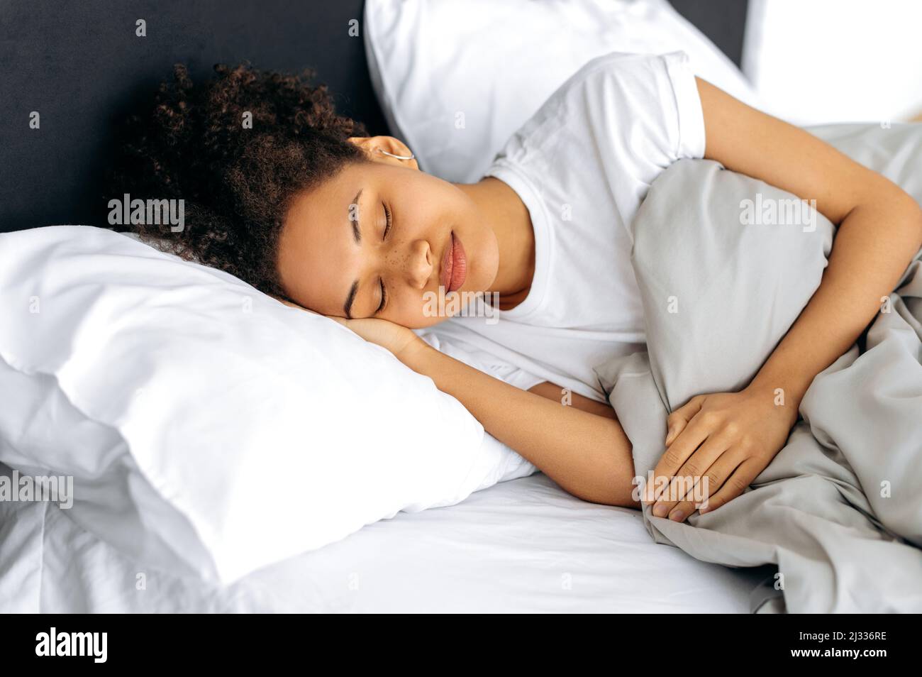 Morning in bed, sweet dreams. Calm African American lovely curly girl, sleeps sweetly in bed, sees dreams, rests, does not want to wake up and get out of bed. Sleep and rest concept Stock Photo