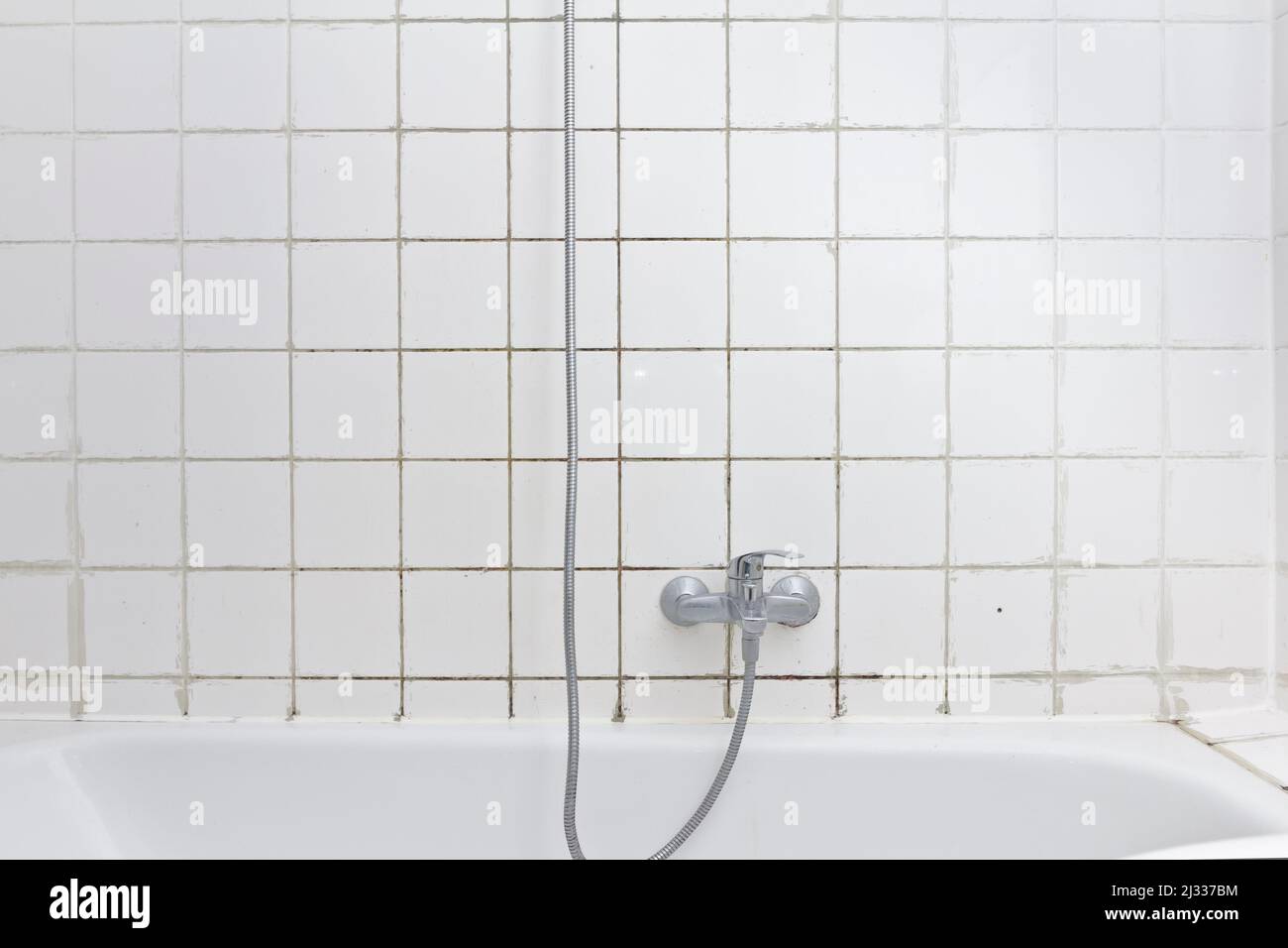 Rental damage concept: grimy shower in bath tub with black mold growing on calcifications on the tile grouting in a neglected old bathroom. Stock Photo