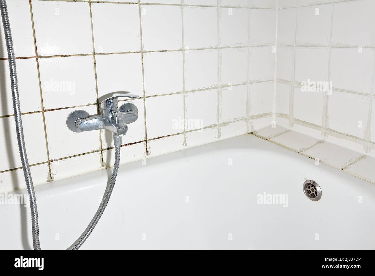 Spring cleaning concept: filthy shower armature in bath tub with black mold growing on calcifications on the tile grouting in an unclean old bathroom. Stock Photo