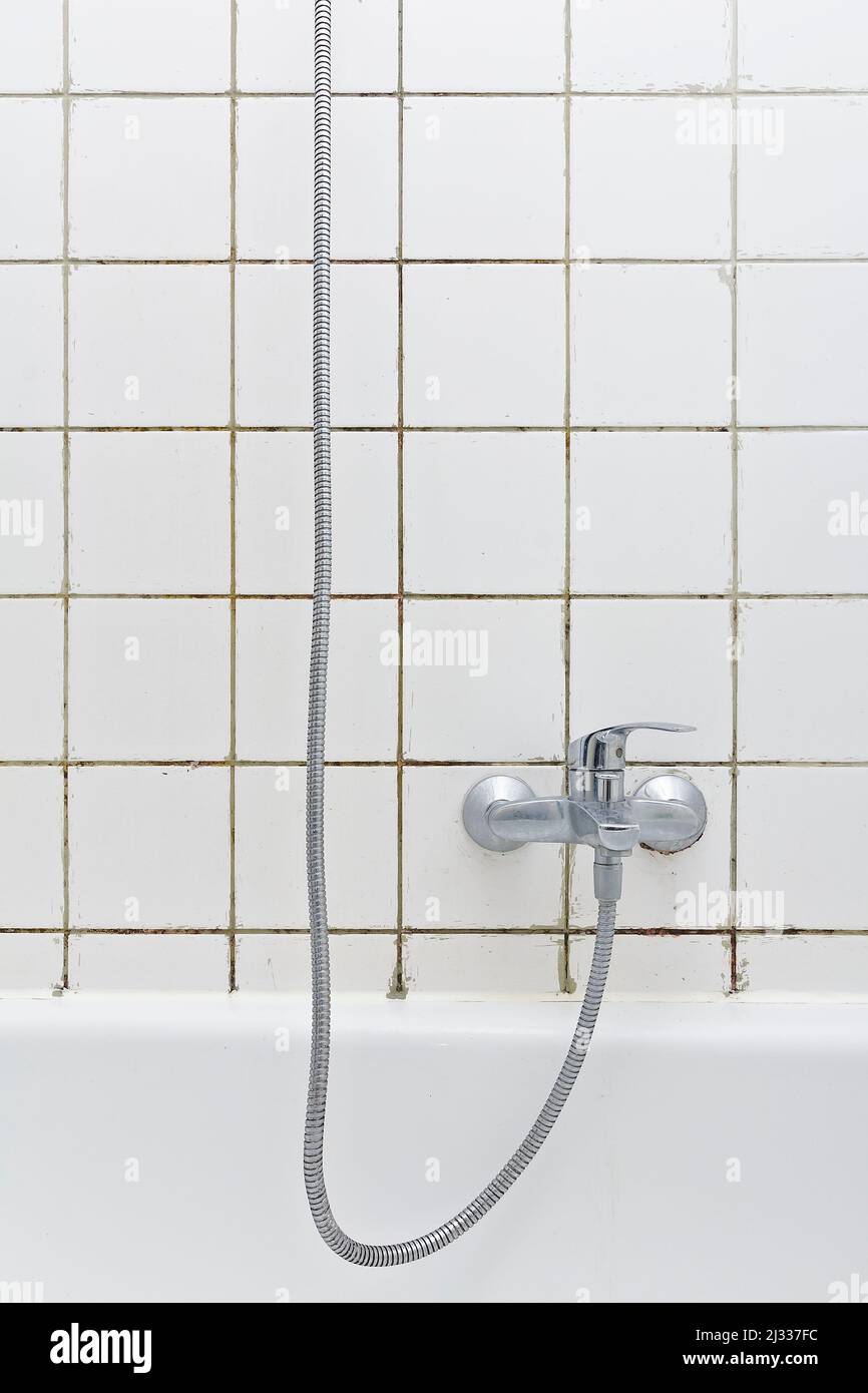 Rental damage concept: grimy shower in bath tub with black mold growing on calcifications on the tile grouting in a neglected old bathroom. Stock Photo