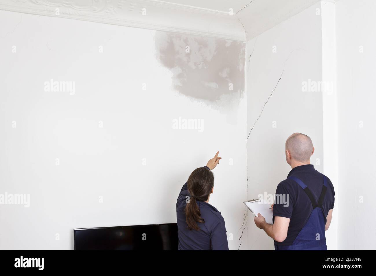 Owner showing a repairman or plumber a big water stain and various cracks in wall and ceiling of her living room in an old building. Stock Photo