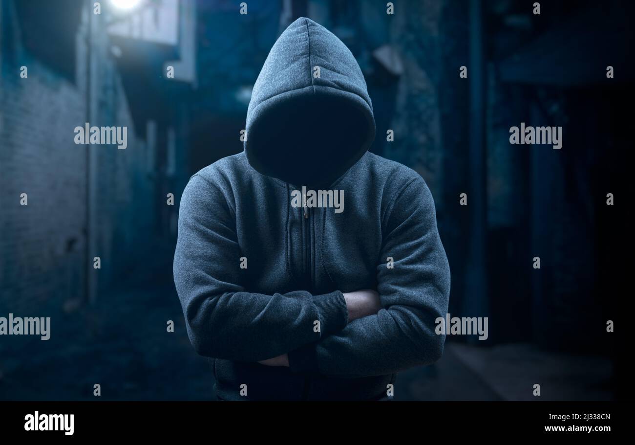 dangerous criminal. scary hooded man at night in dark alley. silhouette bandit, criminal with an unrecognizable face in threatening pose at night on d Stock Photo
