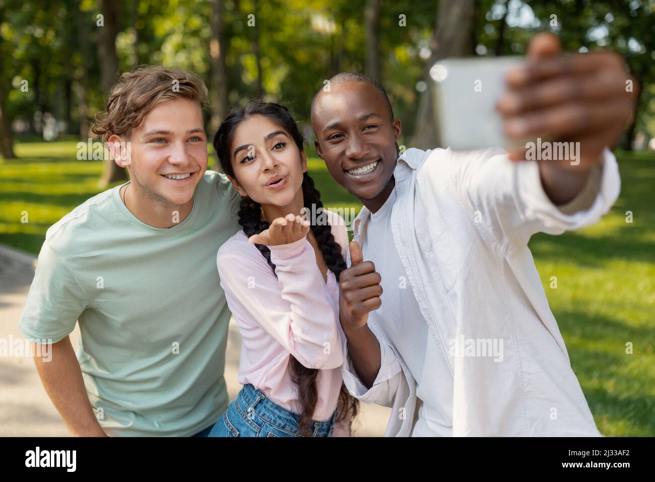 Student's selfie. Happy diverse university friends taking self-portrait on smartphone outdoors and sincerely smiling Stock Photo