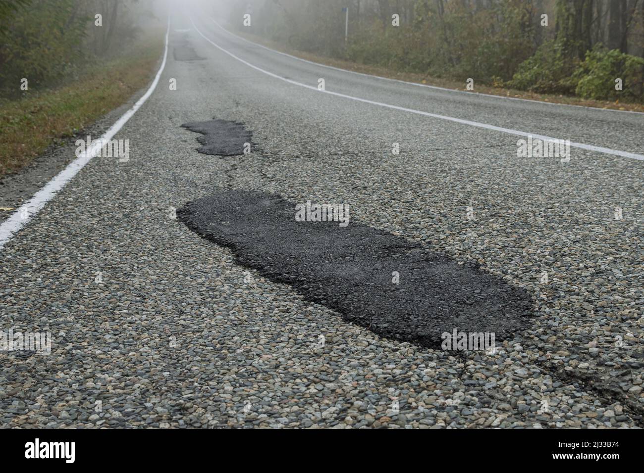 Fresh patches after patching the road. Country highway in the foggy forest. Bad road condition Stock Photo