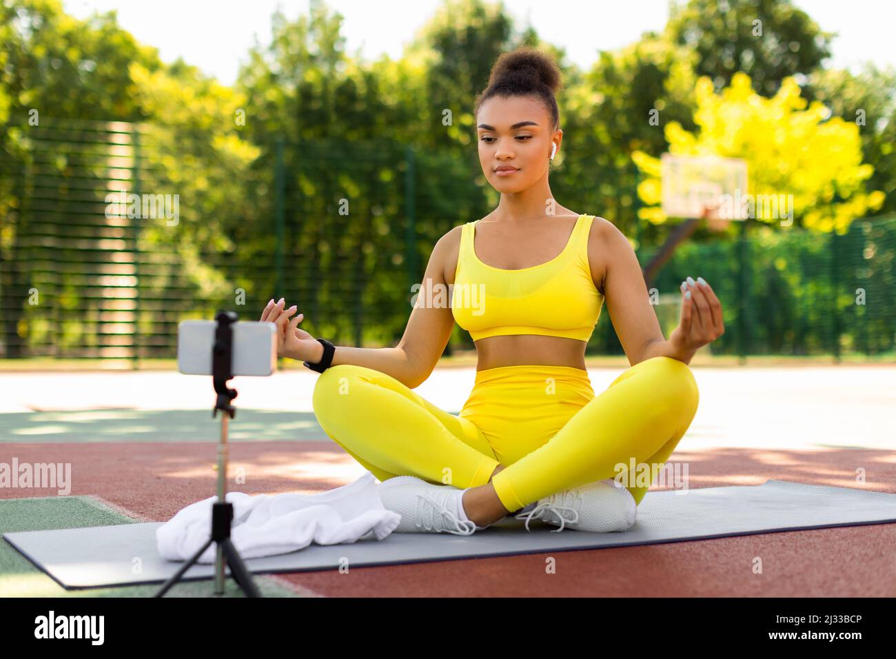 Young woman meditating sitting in front of smartphone outdoors Stock Photo