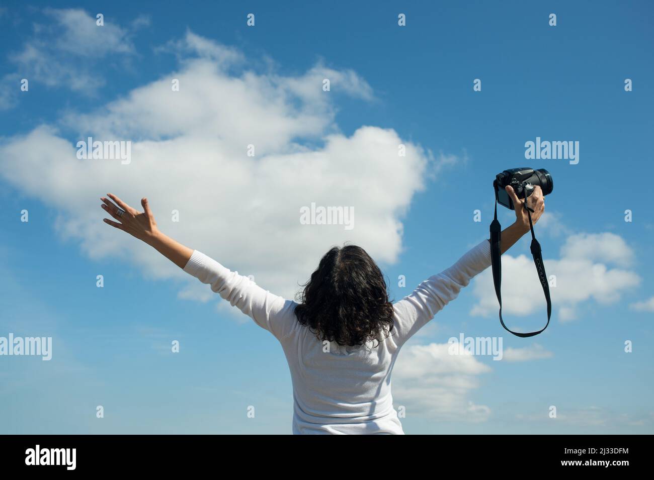 Woman photographer excited about career possibilities. Happy woman photographer with arms extended and camera in one hand. Stock Photo