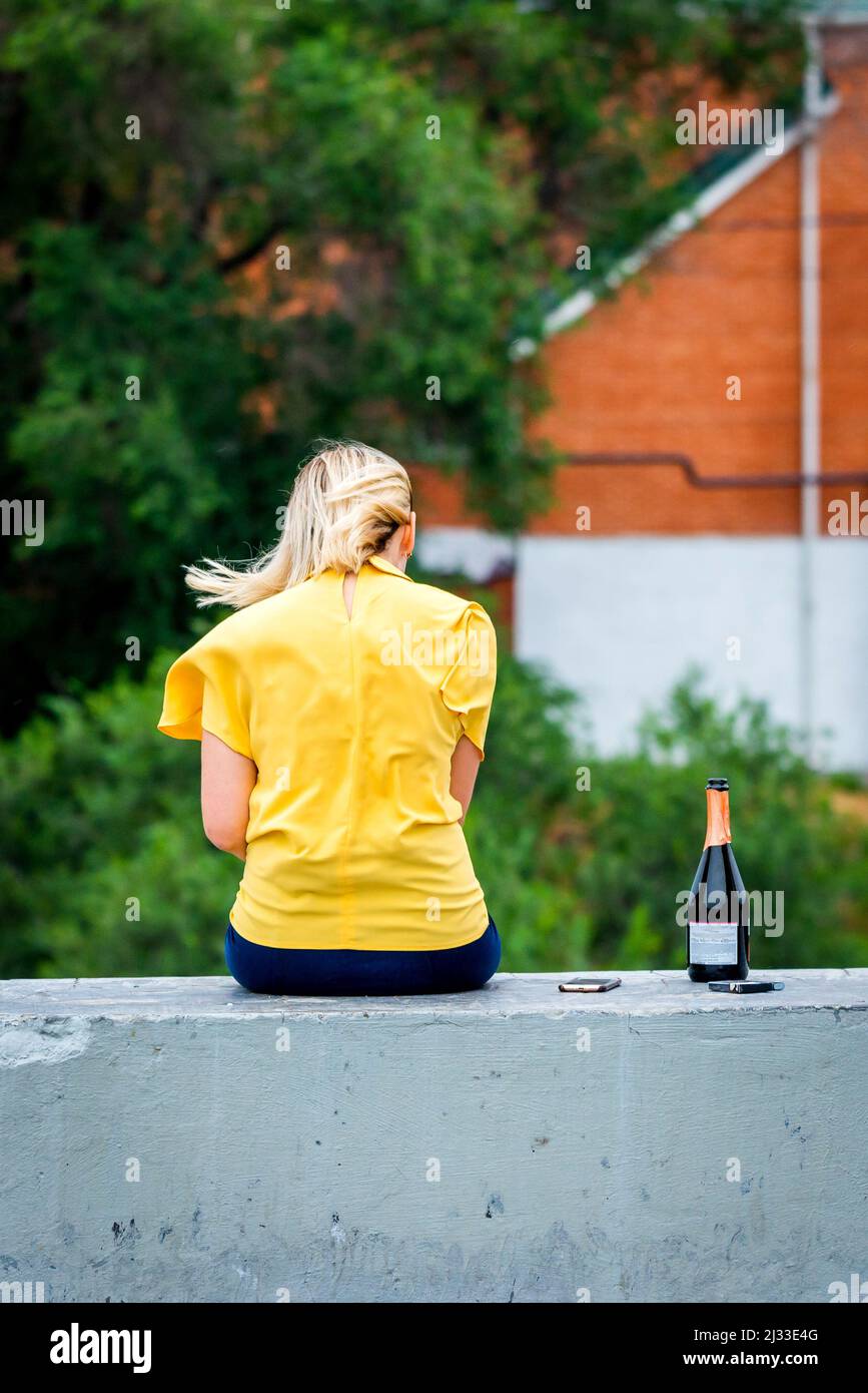 Back view of beautiful blonde girl. Near with her bottle of alcohol and