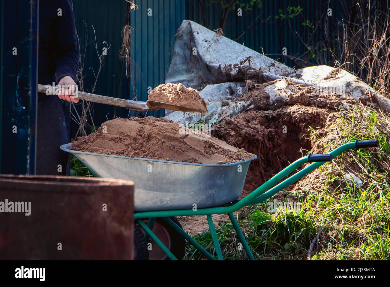 Man uses shovel and fills wheelbarrow with sand. Construction works close-up. Rural life in countryside. Stock Photo