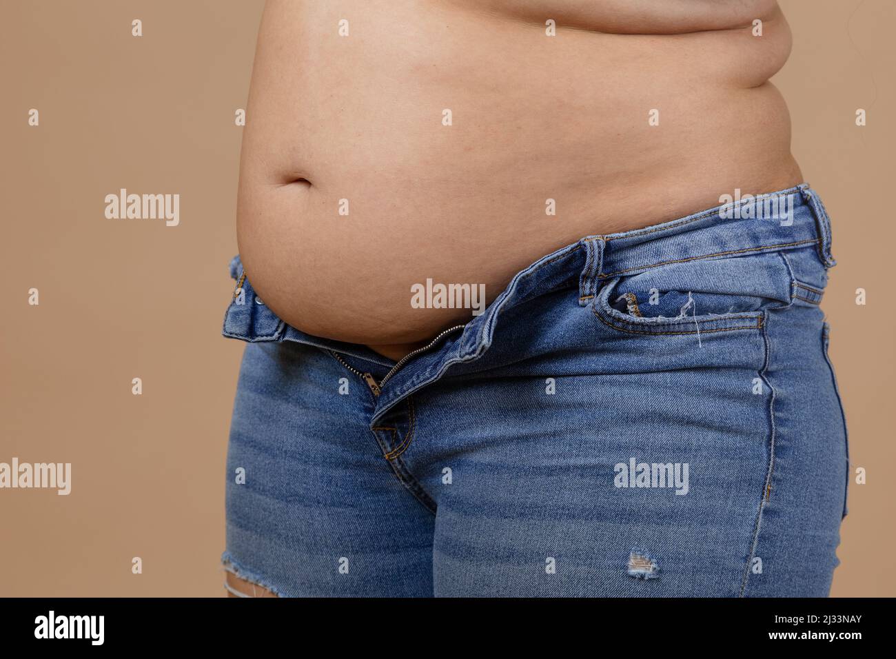 Woman with flabby belly and thick sides showing waist in unzipped jeans of blue color. Sudden weight gain. Visceral fat. Body positive. Tight little Stock Photo